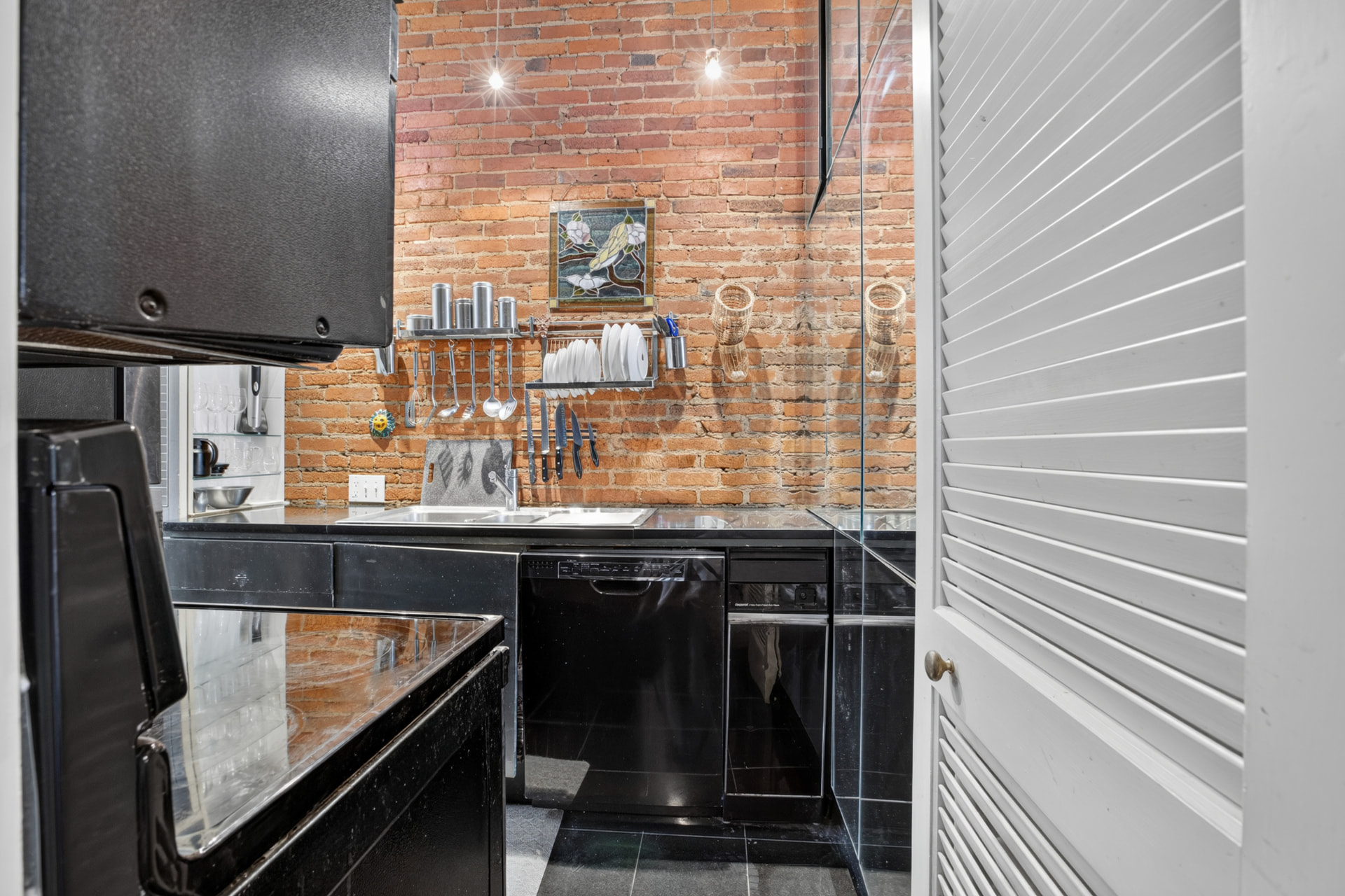 Galley kitchen with full height exposed brick wall, stained glass panel and black stone counters